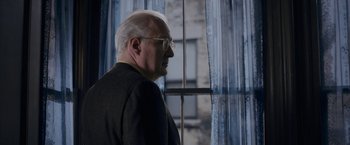 Movie still from “The Woman in the Window” (2021), directed by Joe Wright – An older man wearing glasses standing in front of a window; Close Up shot, Over the shoulder angle