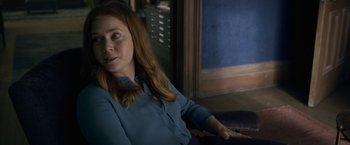 Movie still from “The Woman in the Window” (2021), directed by Joe Wright – A woman sitting on a chair in a room; Medium shot, Over the shoulder angle