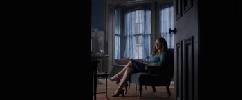 Movie still from “The Woman in the Window” (2021), directed by Joe Wright – A woman sitting on a chair in a room; Wide shot, Low angle