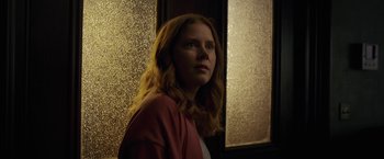 Movie still from “The Woman in the Window” (2021), directed by Joe Wright – A woman with long red hair wearing a pink jacket; Medium shot, Low angle