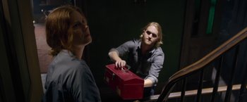 Movie still from “The Woman in the Window” (2021), directed by Joe Wright – A man holding a red box in front of a woman; Medium shot, Over the shoulder angle
