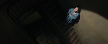 Movie still from “The Woman in the Window” (2021), directed by Joe Wright – A woman standing on the bottom of a set of stairs; Wide shot, Overhead angle