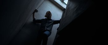 Movie still from “The Woman in the Window” (2021), directed by Joe Wright – A man standing on a staircase holding a remote control; Medium shot, Overhead angle