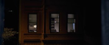 Movie still from “The Woman in the Window” (2021), directed by Joe Wright – A room with two windows at night with a person sitting at a desk in the window; Extreme Wide shot, High angle