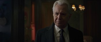 Movie still from “The Woman in the Window” (2021), directed by Joe Wright – An older man with white hair wearing a suit and tie; Close Up shot, Over the shoulder angle