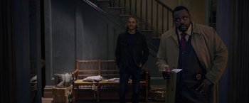 Movie still from “The Woman in the Window” (2021), directed by Joe Wright – A man standing in front of a bench in a room; Medium shot, Over the shoulder angle