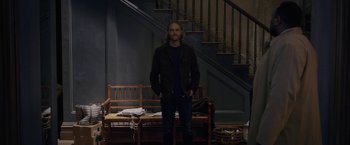 Movie still from “The Woman in the Window” (2021), directed by Joe Wright – A man standing in front of a bench in a room; Wide shot, Low angle