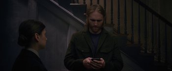 Movie still from “The Woman in the Window” (2021), directed by Joe Wright – A man standing on stairs looking at his phone; Medium shot, High angle