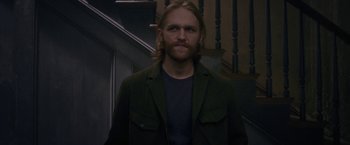 Movie still from “The Woman in the Window” (2021), directed by Joe Wright – A man with long hair wearing a green jacket; Medium shot, Over the shoulder angle