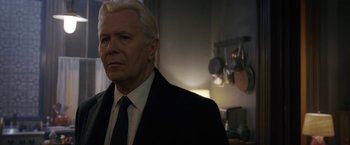 Movie still from “The Woman in the Window” (2021), directed by Joe Wright – A man in a suit and tie in a kitchen; Close Up shot, Over the shoulder angle