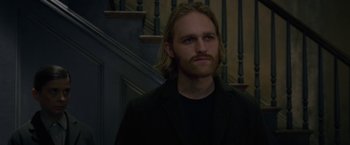 Movie still from “The Woman in the Window” (2021), directed by Joe Wright – A man with long blonde hair standing in front of a staircase; Close Up shot, Low angle
