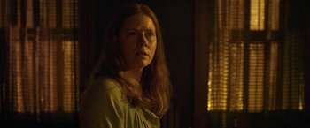 Movie still from “The Woman in the Window” (2021), directed by Joe Wright – A woman with red hair is standing in the dark; Close Up shot, Low angle