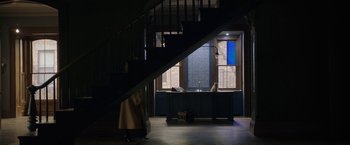 Movie still from “The Woman in the Window” (2021), directed by Joe Wright – A woman walking up a staircase in a dark room; Extreme Wide shot, High angle