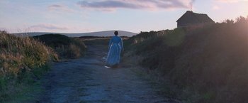 Movie still from “The Wonder” (2022), directed by Sebastián Lelio – A woman in a blue dress walking down a dirt road; Extreme Wide shot, Low angle