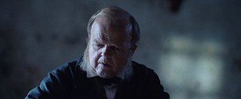 Movie still from “The Wonder” (2022), directed by Sebastián Lelio – An old man with a beard and a bow tie; Close Up shot, Over the shoulder angle