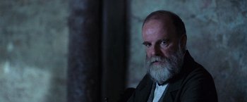 Movie still from “The Wonder” (2022), directed by Sebastián Lelio – An older man with a beard and a mustache; Close Up shot, Over the shoulder angle
