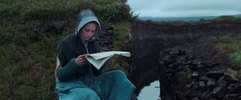 Movie still from “The Wonder” (2022), directed by Sebastián Lelio – A woman sitting on the ground reading a book; Medium shot, High angle