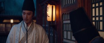 Movie still from “The Yin-Yang Master: Dream of Eternity” (2020), directed by Jingming Guo – A man wearing a hat standing in front of a building; Medium shot, Over the shoulder angle