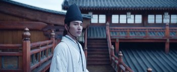 Movie still from “The Yin-Yang Master: Dream of Eternity” (2020), directed by Jingming Guo – A man wearing a hat standing in front of a building; Medium shot, Over the shoulder angle