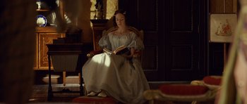 Movie still from “The Young Victoria” (2009), directed by Jean-Marc Vallée – A woman sitting in a chair while reading a book; Wide shot, High angle