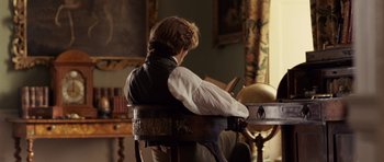 Movie still from “The Young Victoria” (2009), directed by Jean-Marc Vallée – A man sitting in a chair reading a book; Medium shot, Over the shoulder angle
