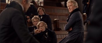Movie still from “The Young Victoria” (2009), directed by Jean-Marc Vallée – A group of men sitting on steps in front of a wooden staircase; Medium shot, Over the shoulder angle