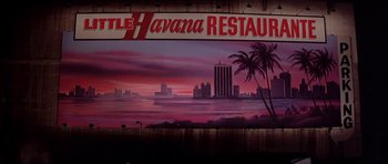 Movie still from “Scarface” (1983), directed by Brian De Palma – A restaurant sign with a view of the ocean and palm trees in the background; Extreme Wide shot, Low angle