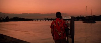 Movie still from “Scarface” (1983), directed by Brian De Palma – A man standing next to a phone booth near a body of water; Extreme Wide shot, Low angle