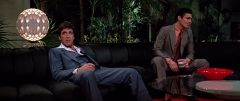 Movie still from “Scarface” (1983), directed by Brian De Palma – Two men in suits sitting on a black couch; Wide shot, Low angle