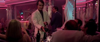 Movie still from “Scarface” (1983), directed by Brian De Palma – A man pouring wine into a wine glass at a party; Medium shot, Over the shoulder angle