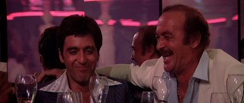 Movie still from “Scarface” (1983), directed by Brian De Palma – A couple of men sitting next to each other at a table; Close Up shot, Low angle