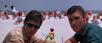 Movie still from “Scarface” (1983), directed by Brian De Palma – Two men sitting on the beach with a drink; Close Up shot, High angle