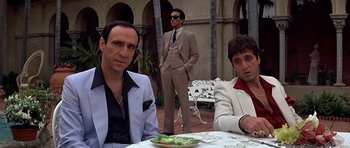 Movie still from “Scarface” (1983), directed by Brian De Palma – A group of men sitting at a table in front of a building; Medium shot, Low angle