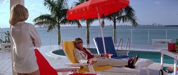 Movie still from “Scarface” (1983), directed by Brian De Palma – A woman sitting on a chair under an umbrella; Wide shot, Low angle