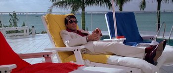 Movie still from “Scarface” (1983), directed by Brian De Palma – A man sitting on a chair on the beach; Wide shot, Low angle