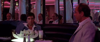 Movie still from “Scarface” (1983), directed by Brian De Palma – A man sitting at a table in front of a mirror; Medium shot, Over the shoulder angle