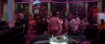 Movie still from “Scarface” (1983), directed by Brian De Palma – A group of people sitting at tables in a room; Wide shot, High angle