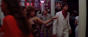 Movie still from “Scarface” (1983), directed by Brian De Palma – A woman pointing at a man in a suit and tie; Medium shot, Over the shoulder angle