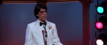 Movie still from “Scarface” (1983), directed by Brian De Palma – A man in a white suit standing in front of a microphone; Close Up shot, Low angle