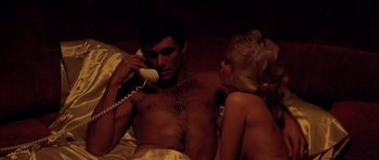 Movie still from “Scarface” (1983), directed by Brian De Palma – A man and a woman laying in a bed talking on a phone; Medium shot, High angle