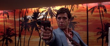 Movie still from “Scarface” (1983), directed by Brian De Palma – A man holding a gun while standing in front of palm trees; Close Up shot, Low angle