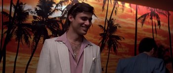 Movie still from “Scarface” (1983), directed by Brian De Palma – A young man wearing a suit and tie smiling for the camera; Close Up shot, Over the shoulder angle