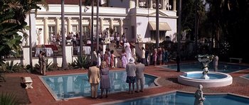 Movie still from “Scarface” (1983), directed by Brian De Palma – A group of people standing around a pool of water; Extreme Wide shot, High angle