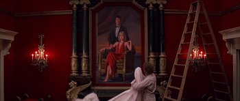 Movie still from “Scarface” (1983), directed by Brian De Palma – A woman sitting in front of a painting of a man and a woman; Wide shot, Low angle