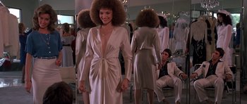 Movie still from “Scarface” (1983), directed by Brian De Palma – A woman in a white dress with a large afro in front of a mirror; Medium shot, Low angle
