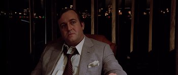 Movie still from “Scarface” (1983), directed by Brian De Palma – A man in a suit and tie sitting in a chair; Close Up shot, Low angle