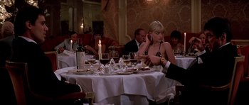 Movie still from “Scarface” (1983), directed by Brian De Palma – A group of people sitting around a table with wine glasses; Medium shot, Over the shoulder angle