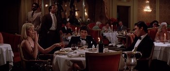 Movie still from “Scarface” (1983), directed by Brian De Palma – A group of people sitting at a dinner table; Wide shot, Over the shoulder angle