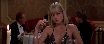 Movie still from “Scarface” (1983), directed by Brian De Palma – A woman sitting at a table with a cigarette in her hand; Close Up shot, Low angle