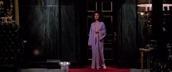 Movie still from “Scarface” (1983), directed by Brian De Palma – A woman standing in front of a door wearing a purple robe; Wide shot, Low angle